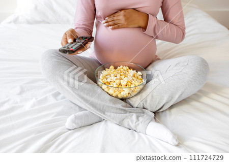 Cropped Shot Of Pregnant Woman With Popcorn And Remote Controller In Hands Cropped Shot Of Pregnant Woman With Popcorn And Remote Controller In Hands 111724729