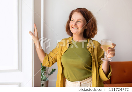 Relaxed senior woman holding glass of wine ad looking from window Relaxed senior woman holding glass of wine ad looking from window 111724772