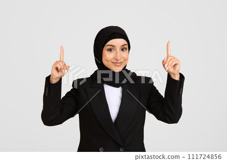 Smiling young businesswoman in hijab pointing upwards Smiling young businesswoman in hijab pointing upwards 111724856