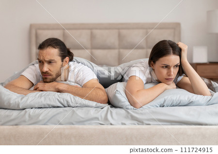 Couple in bed with worried expressions facing away 111724915