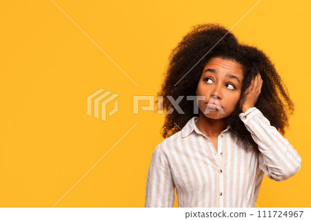 Pensive black woman with hand in hair on yellow background Pensive black woman with hand in hair on yellow background 111724967