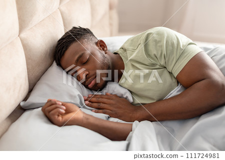 Sleeping black guy enjoying peaceful restful nap lying in bed Sleeping black guy enjoying peaceful restful nap lying in bed 111724981