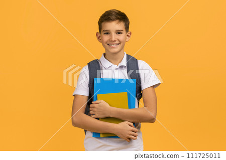 Smiling teen schoolboy with backpack holding textbooks and smiling at camera 111725011