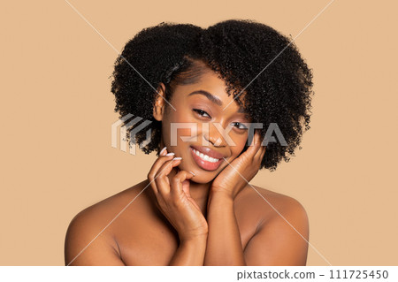 Content black woman with hands on face, curly hair, beige background 111725450