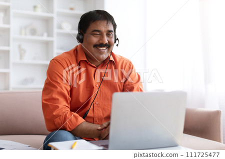 Excited mature indian man with headset using laptop at home Excited mature indian man with headset using laptop at home 111725477