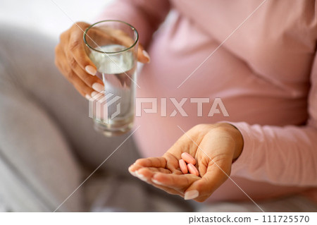 Prenatal Vitamins And Supplements. Unrecognizable black pregnant woman taking pills at home Prenatal Vitamins And Supplements. Unrecognizable black pregnant woman taking pills at home 111725570