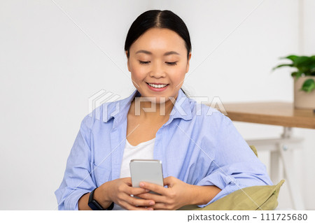 Positive korean lady enjoying weekend at home, using smartphone Positive korean lady enjoying weekend at home, using smartphone 111725680