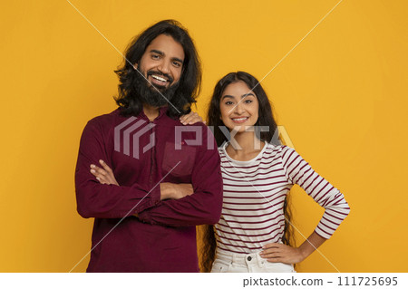 Positive young indian man and woman posing on yellow background 111725695