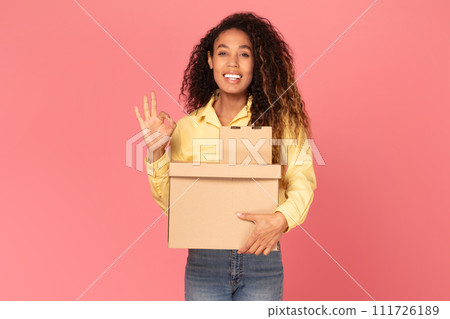 Young black woman holding parcel, gesturing okay on pink background Young black woman holding parcel, gesturing okay on pink background 111726189