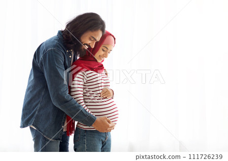 Loving arab man hugging his pregnant muslim wife's belly at home 111726239