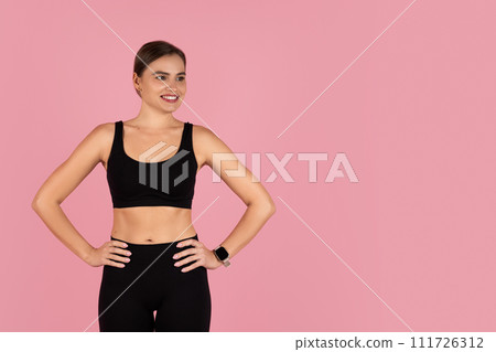 Smiling woman dressed in black workout clothes standing with hands on hips 111726312