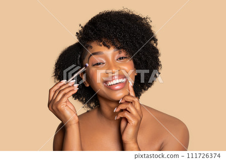 Happy african american woman applying eyeshadow, doing nude makeup Happy african american woman applying eyeshadow, doing nude makeup 111726374