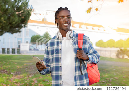black university student guy with headphones using smartphone on campus 111726494