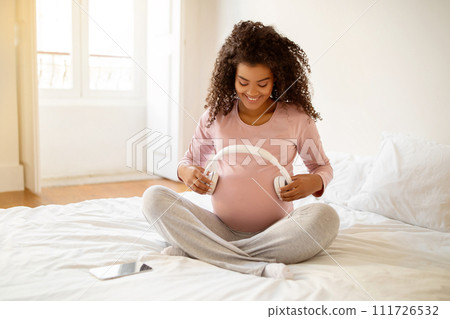 Pregnant Woman Holding Headphones Near Belly, Playing Melody To Baby In Womb Pregnant Woman Holding Headphones Near Belly, Playing Melody To Baby In Womb 111726532
