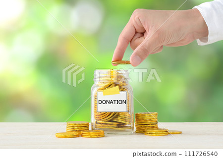 Hand of a person putting donations into a jar with the word DONATION written on it 111726540