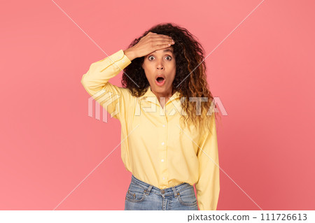 Shocked black woman with hand on forehead, wide-eyed, on pink background 111726613