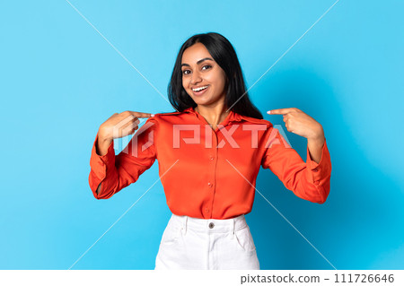 Happy young indian lady pointing fingers at herself, blue background 111726646
