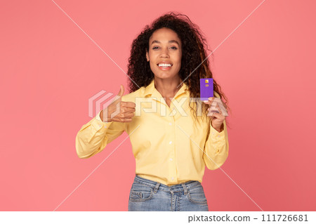 Happy black woman with credit card gesturing thumbs up on pink backdrop 111726681