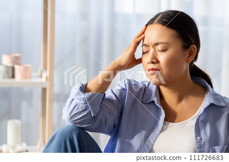 Asian woman with closed eyes touching her head Asian woman with closed eyes touching her head 111726683