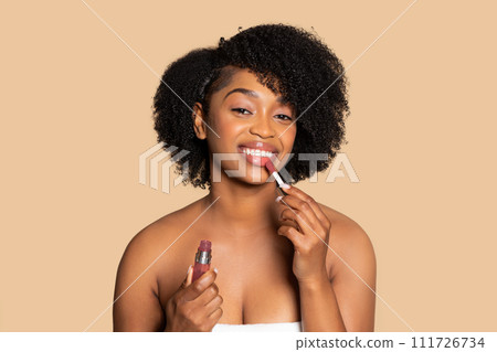 Happy black woman applying lip gloss with smile 111726734