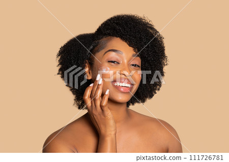 Radiant black woman with curly hair applying cream on face 111726781
