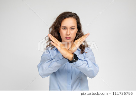 A determined young woman in a blue shirt makes an X sign with her arms 111726796