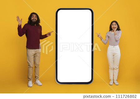 Excited young indian couple pointing at huge smartphone 111726802