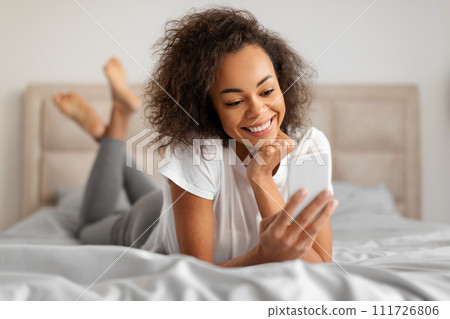 Smiling African American Young Woman Texting Using Mobile Phone Indoor Smiling African American Young Woman Texting Using Mobile Phone Indoor 111726806
