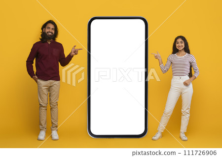 Smiling young indian couple pointing at huge smartphone 111726906