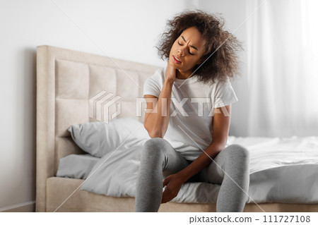 Tired african american millennial woman touching aching neck in bedroom Tired african american millennial woman touching aching neck in bedroom 111727108