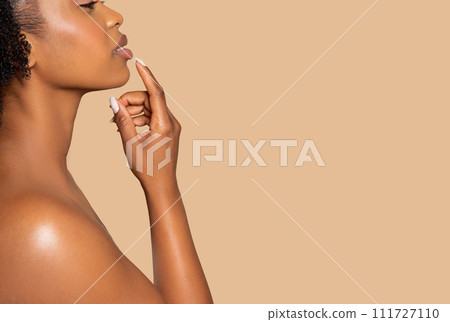 Profile shot of black woman touching lips, soft beige background Profile shot of black woman touching lips, soft beige background 111727110