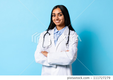 Portrait Of Cheerful Middle Eastern Young Doctor Woman, Blue Background Portrait Of Cheerful Middle Eastern Young Doctor Woman, Blue Background 111727279