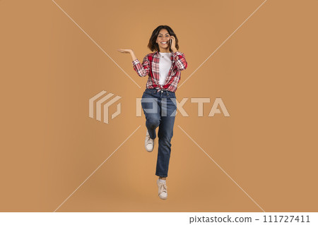 Emotional happy young arab woman jumping and talking on phone 111727411