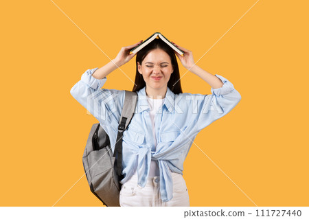 Tired female student with book on head and backpack Tired female student with book on head and backpack 111727440