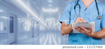 A focused male nurse in blue scrubs is using a tablet to record medical data 111727468