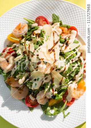 Fresh salad with greens, tomatoes, grilled shrimps on white plate. Top view on yellow background. Fresh salad with greens, tomatoes, grilled shrimps on white plate. Top view on yellow background. 111727668