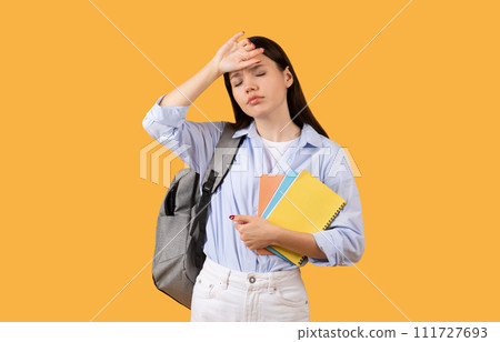 Exhausted student with copybooks and backpack over yellow background 111727693