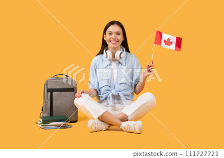 Smiling female student with Canadian flag and headphones on yellow Smiling female student with Canadian flag and headphones on yellow 111727721