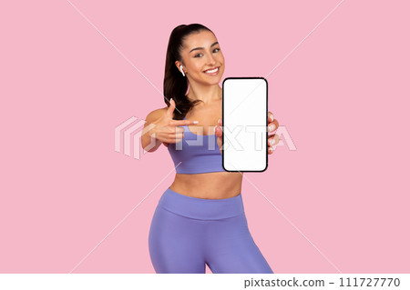 Cheerful woman showing smartphone screen, wearing gym clothes 111727770