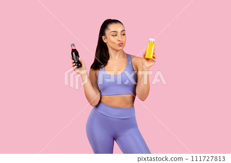 Fitness woman comparing drinks against pink background 111727813