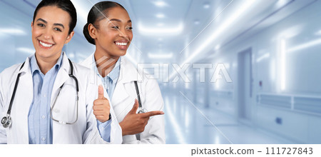 Two happy healthcare workers in white lab coats give a thumbs up in a hospital corridor 111727843