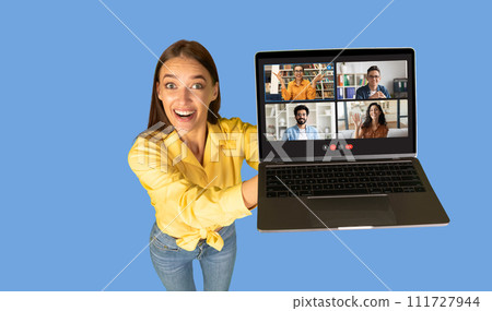 A joyful woman in a yellow blouse extends her arm to present a laptop screen showing a friendly group video call 111727944