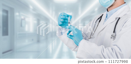A healthcare professional in a white lab coat and surgical mask prepares a vaccine in a syringe A healthcare professional in a white lab coat and surgical mask prepares a vaccine in a syringe 111727998