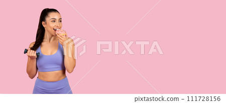 Happy woman with dumbbell eating donut, panorama with free space 111728156