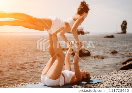 Woman sea yoga. Two happy women practicing yoga on the beach with ocean and rock mountains. Motivation and inspirational fit and exercising. Healthy lifestyle outdoors in nature, fitness concept. 111728430