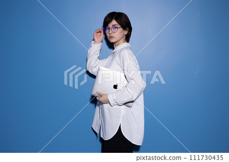 A young woman wearing glasses photographed against a blue background A young woman wearing glasses photographed against a blue background 111730435