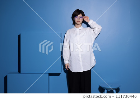A young woman wearing glasses photographed against a blue background A young woman wearing glasses photographed against a blue background 111730446