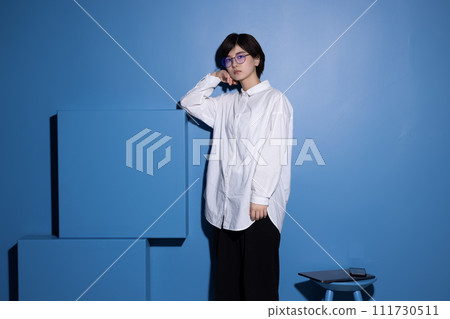 A young woman wearing glasses photographed against a blue background 111730511