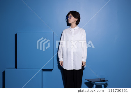 A young woman wearing glasses photographed against a blue background A young woman wearing glasses photographed against a blue background 111730561