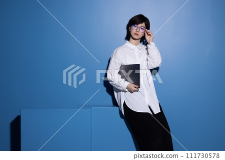 A young woman wearing glasses photographed against a blue background 111730578